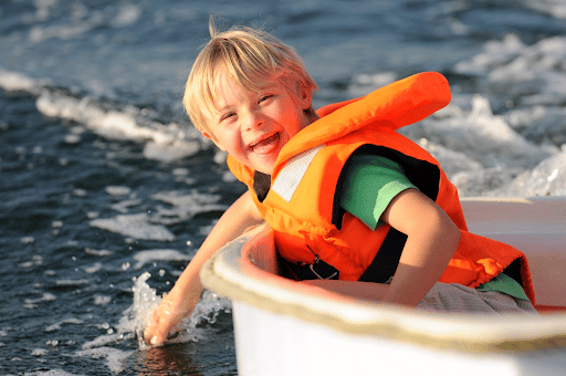 A child wearing his lifejacket while out on a boat with his hand in the water. 