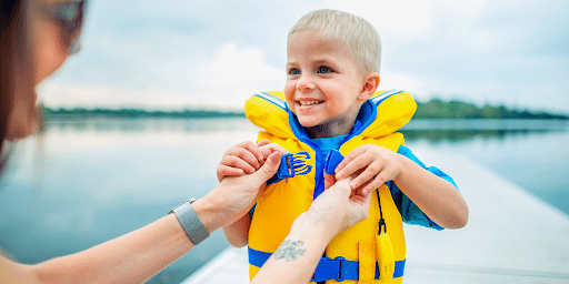 A child on a boat putting on a lifejacket with help from their mother. 